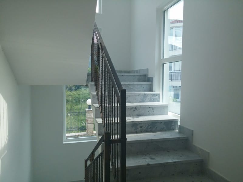 Marble staircase with wrought-iron railings in a house in Đenovići, Montenegro, with panoramic windows and a view of the garden.