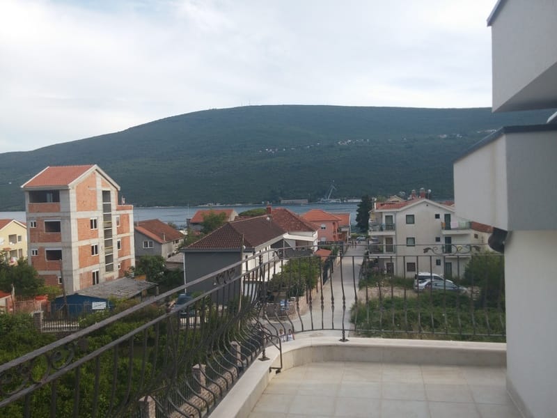 View from a spacious balcony in Đenovići, Montenegro: a panorama of the sea, mountains, and cozy town buildings.