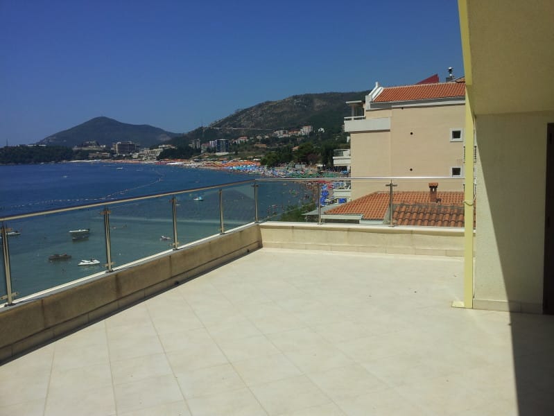 Spacious terrace with panoramic views of the sea and beach in Rafailovici, Montenegro, with modern glass railing.