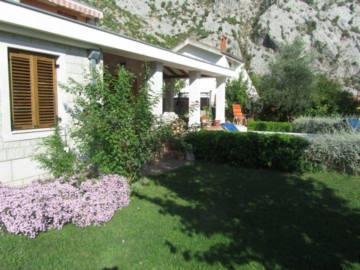 Villa in Orahovac, Montenegro: a stone house with a terrace, a green garden, and a mountain view on a sunny day.