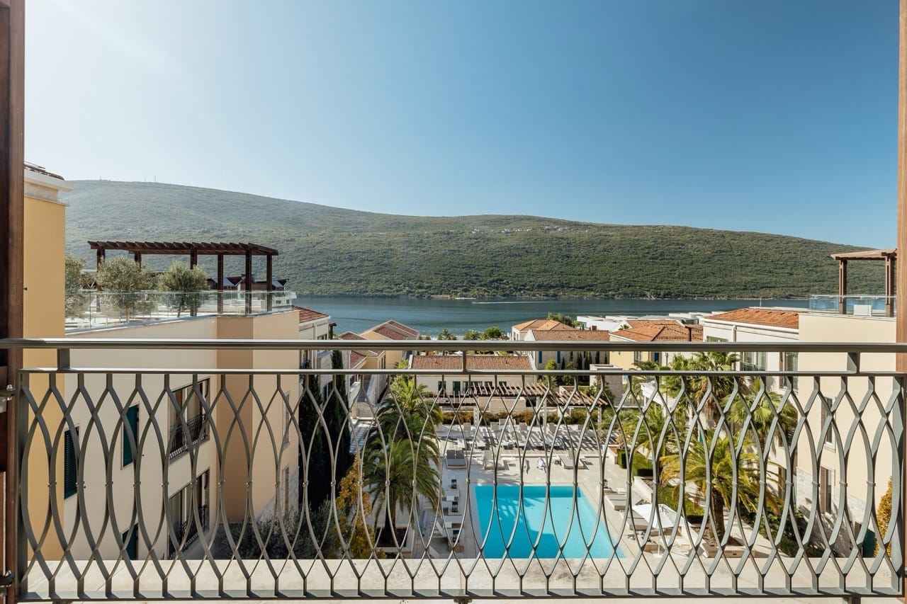 View from the apartment balcony in Portonovi, Kumbor, Montenegro: pool, Mediterranean architecture, and the bay.