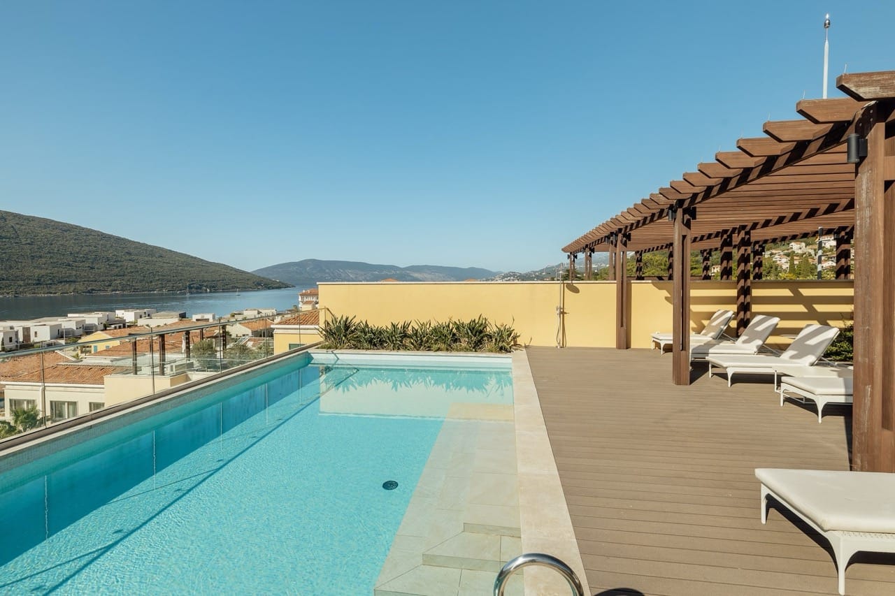 Open-air pool with sea and mountain views on the apartment terrace in Portonovi, Kumbor, Montenegro, with sun loungers and a pergola.