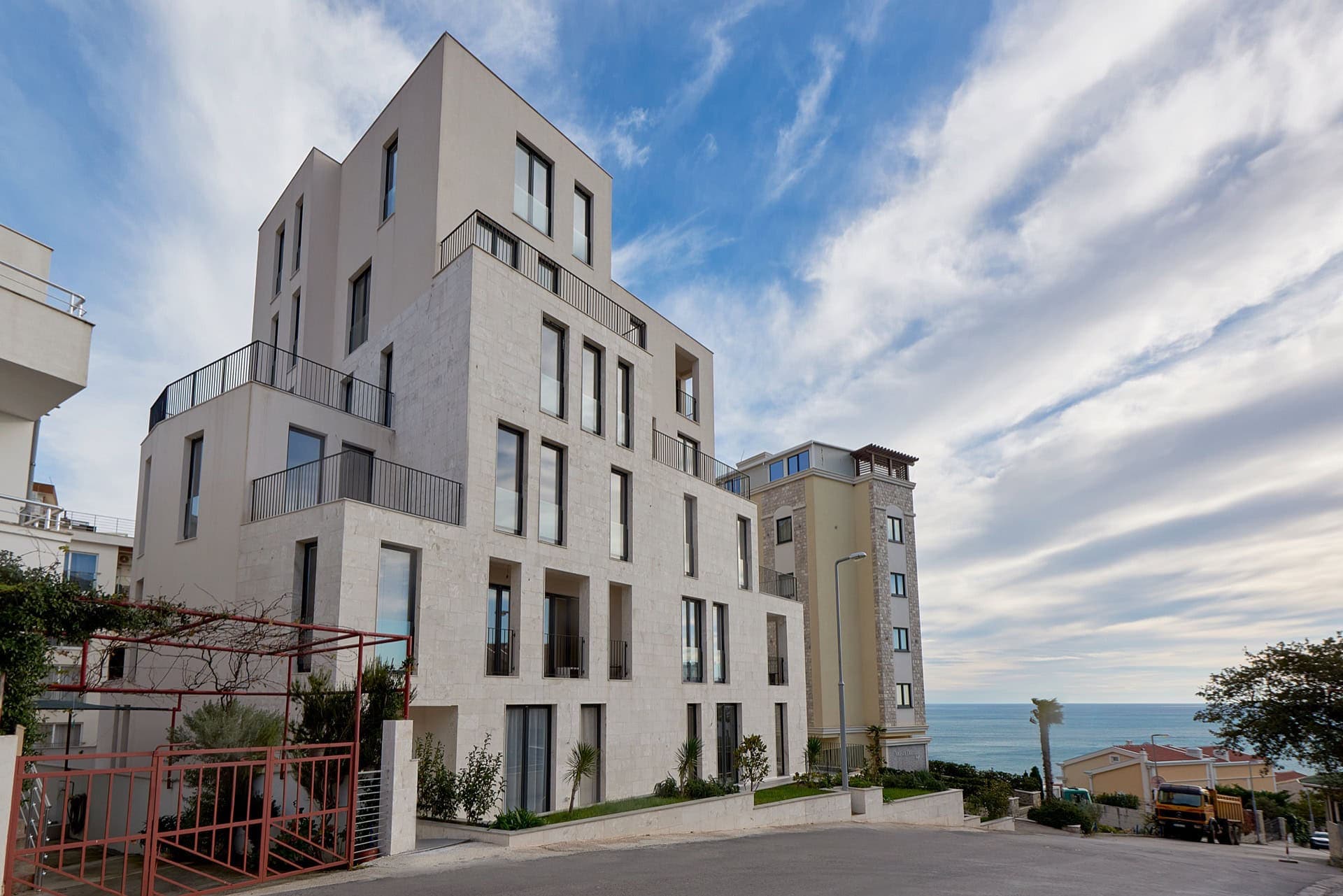 Современный жилой комплекс с террасами в Бечичи, Черногория, вид на море и фасад из светлого камня.