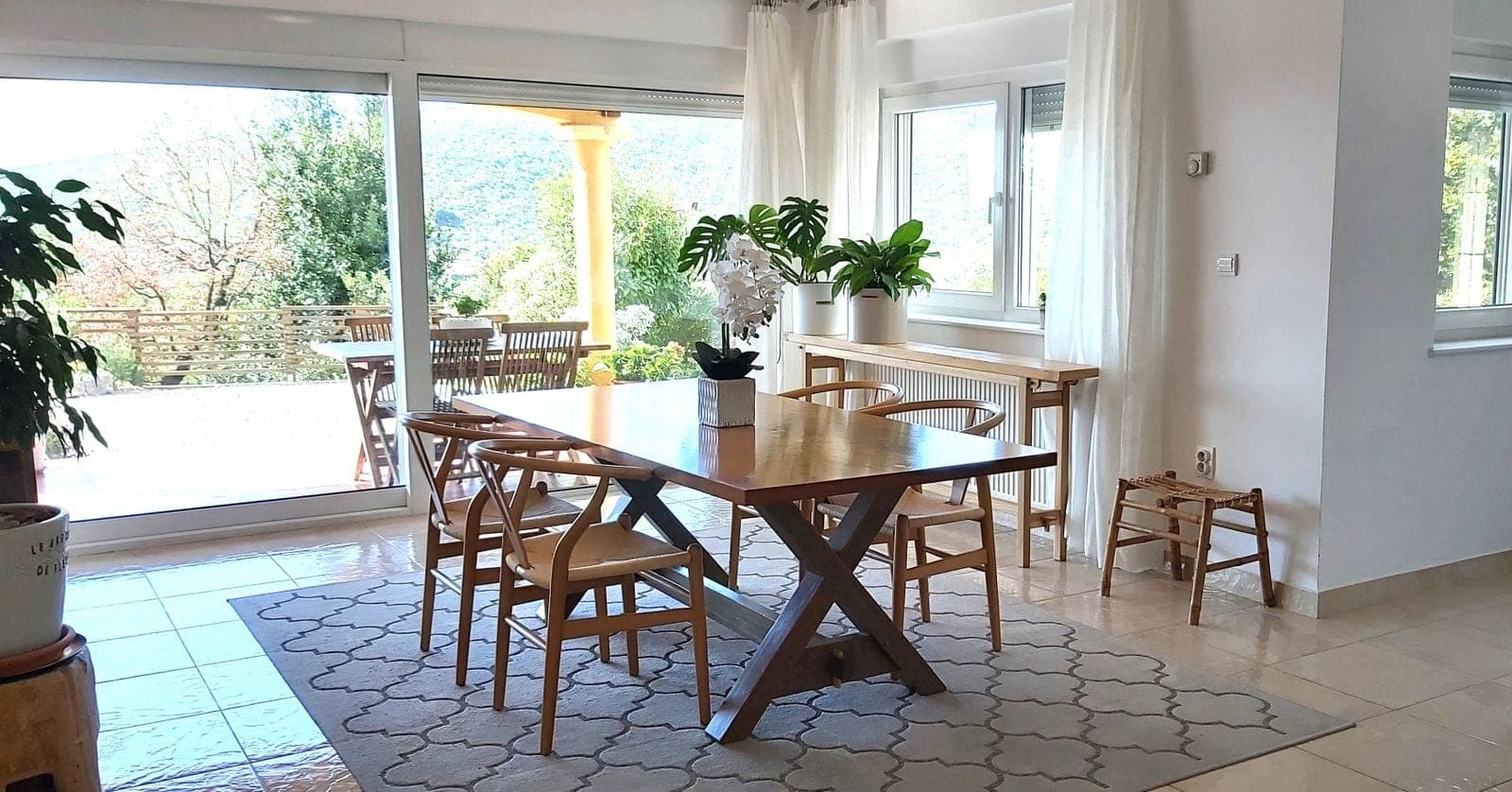 Светлая столовая с деревянным столом и выходом на террасу в доме, Ковачи, Черногория. Панорамные окна и вид на сад.