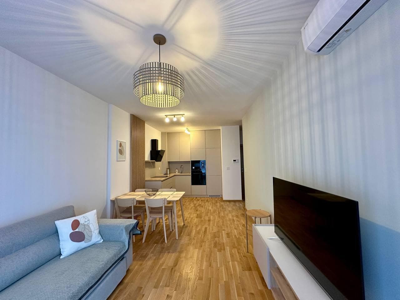 Современная гостиная с кухней в квартире в Бечичи, Черногория: серый диван, обеденная зона и встроенная техника.