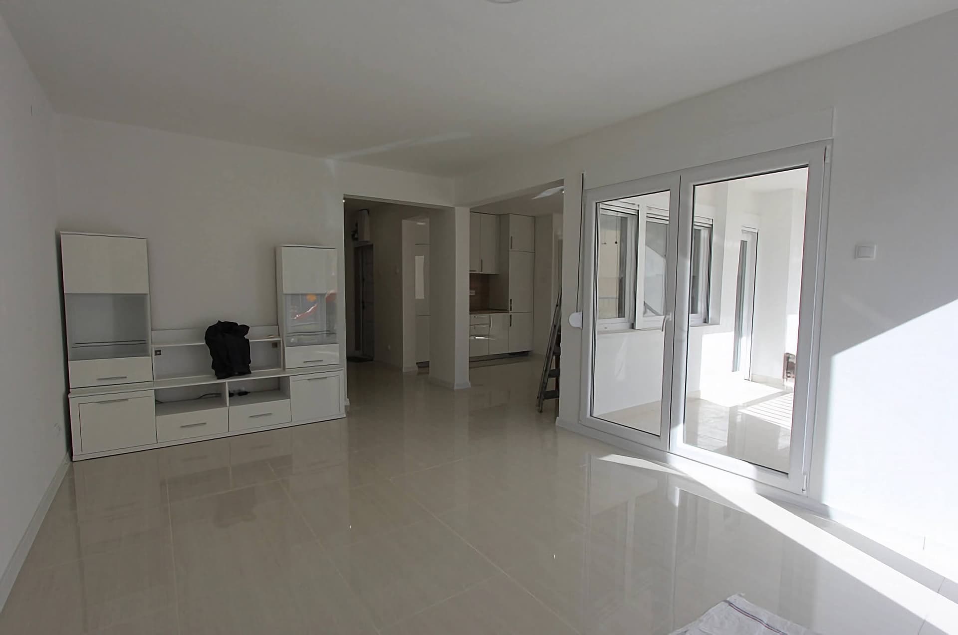 Светлая гостиная с белой мебелью и панорамными окнами в квартире в Тивате, Черногория. Современный интерьер с плиткой.