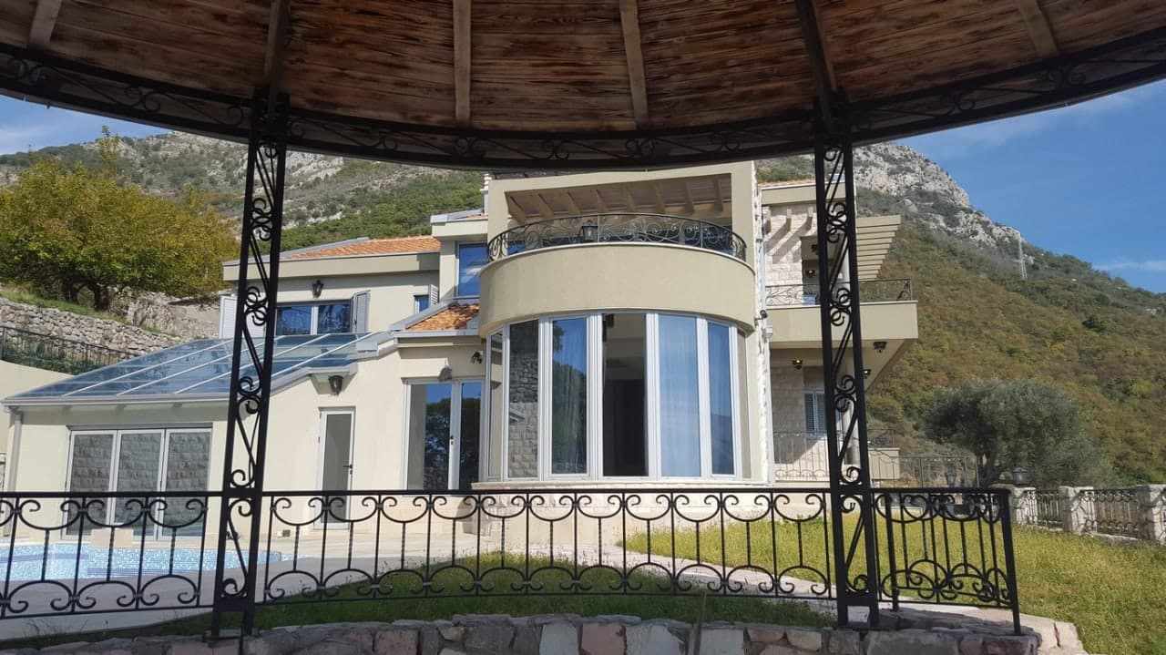 Современная вилла в Баре, Черногория: фасад с панорамными окнами, террасой, бассейном и видом на горы из беседки.