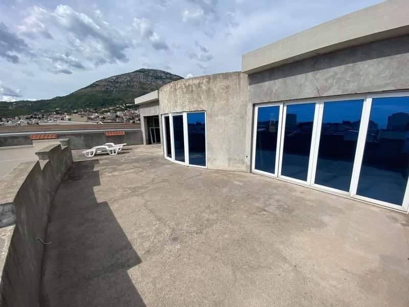 Терраса дома в Шушани, Черногория: панорамные окна, вид на горы, бетонная отделка и шезлонги на крыше объекта.