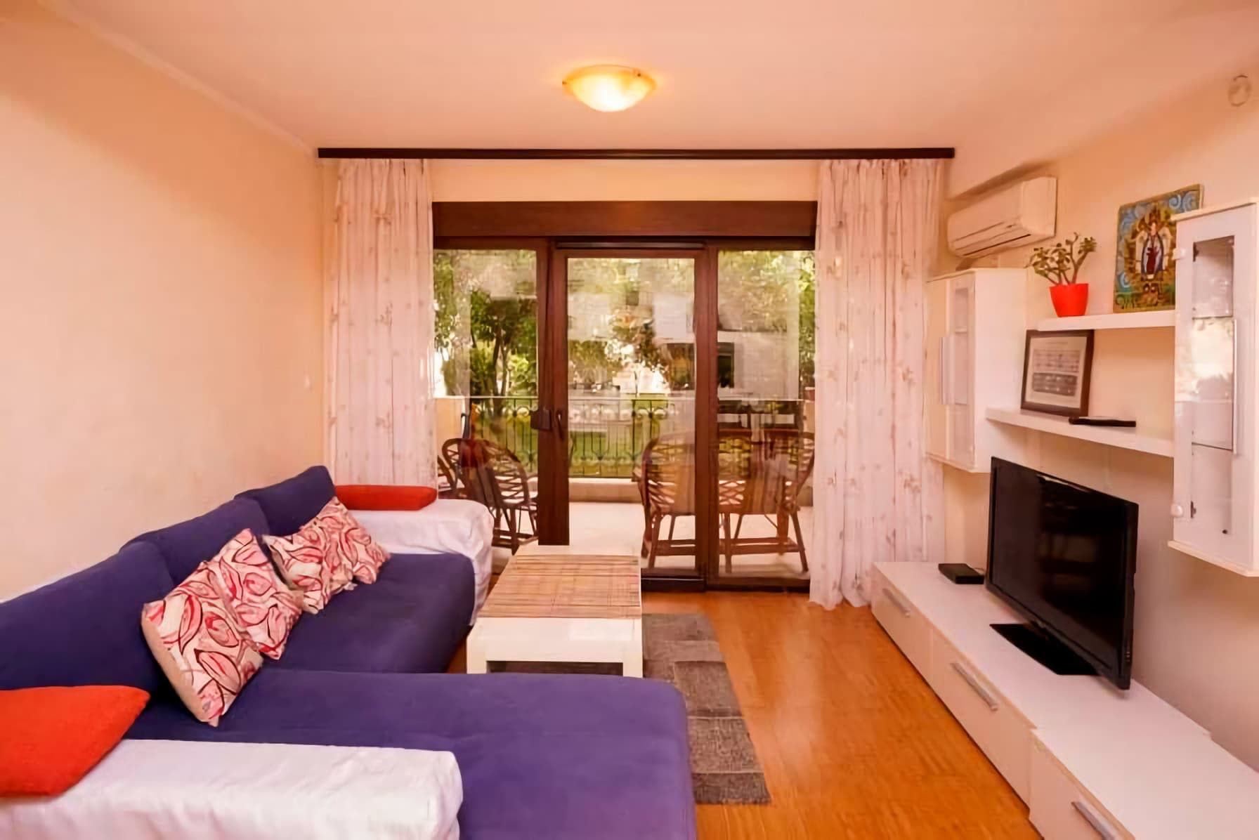 Уютная гостиная с синим диваном и выходом на террасу в квартире в Будве, Черногория. Современный интерьер с ТВ-зоной.