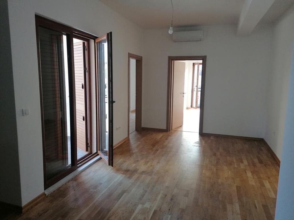 Светлая пустая комната с паркетом, кондиционером и выходом на балкон в квартире, Тиват, Черногория.