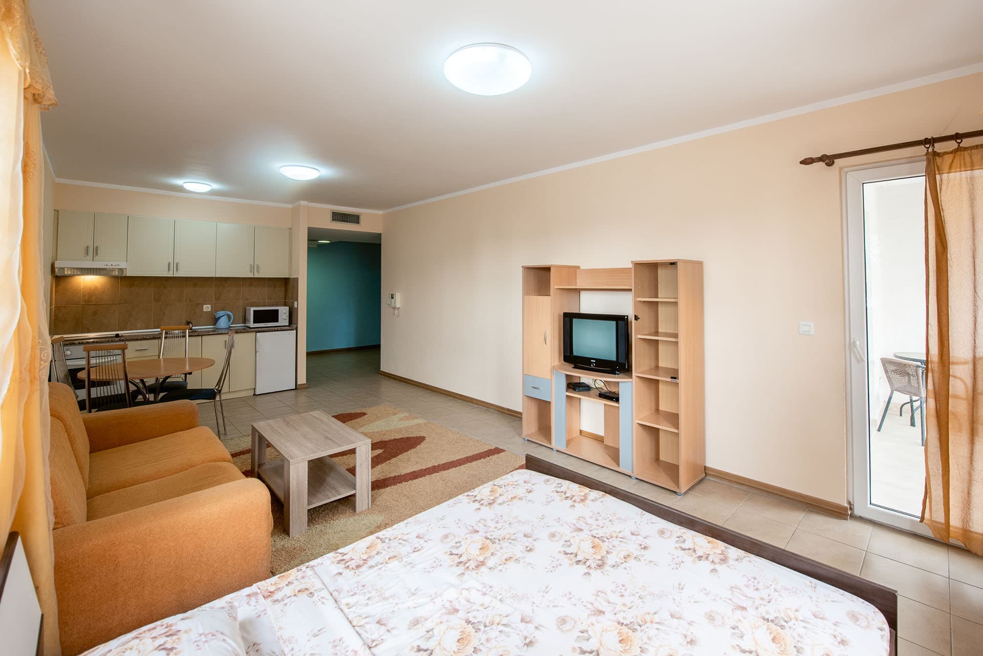 Интерьер квартиры в Бечичи, Черногория: гостиная с кухней, диваном, кроватью, ТВ-зоной и выходом на балкон.