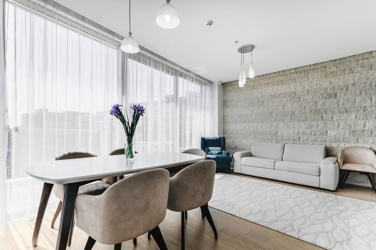 Современная гостиная с обеденной зоной и каменной стеной в квартире в Будве, Черногория. Панорамные окна и стильная мебель.