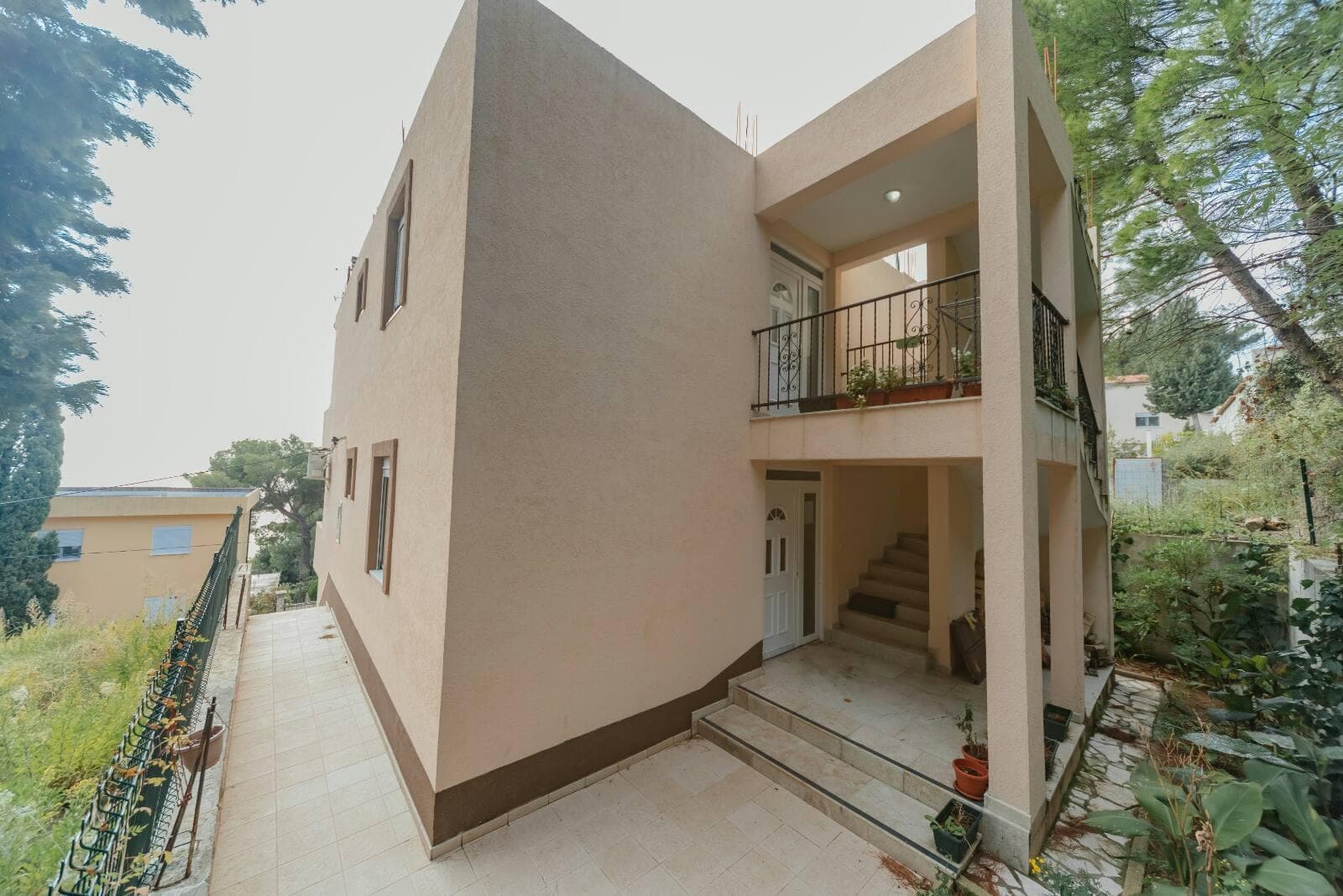 Двухэтажный дом с террасой и лестницей в районе Шушань, Черногория: фасад здания и прилегающая территория.