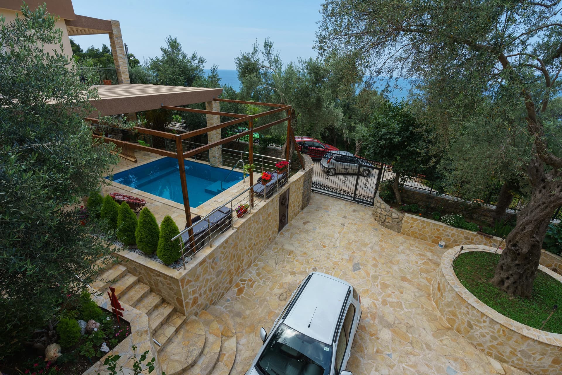 Двор дома в Сутоморе, Черногория: бассейн с террасой, каменная отделка, парковка и вид на море среди оливковых деревьев.