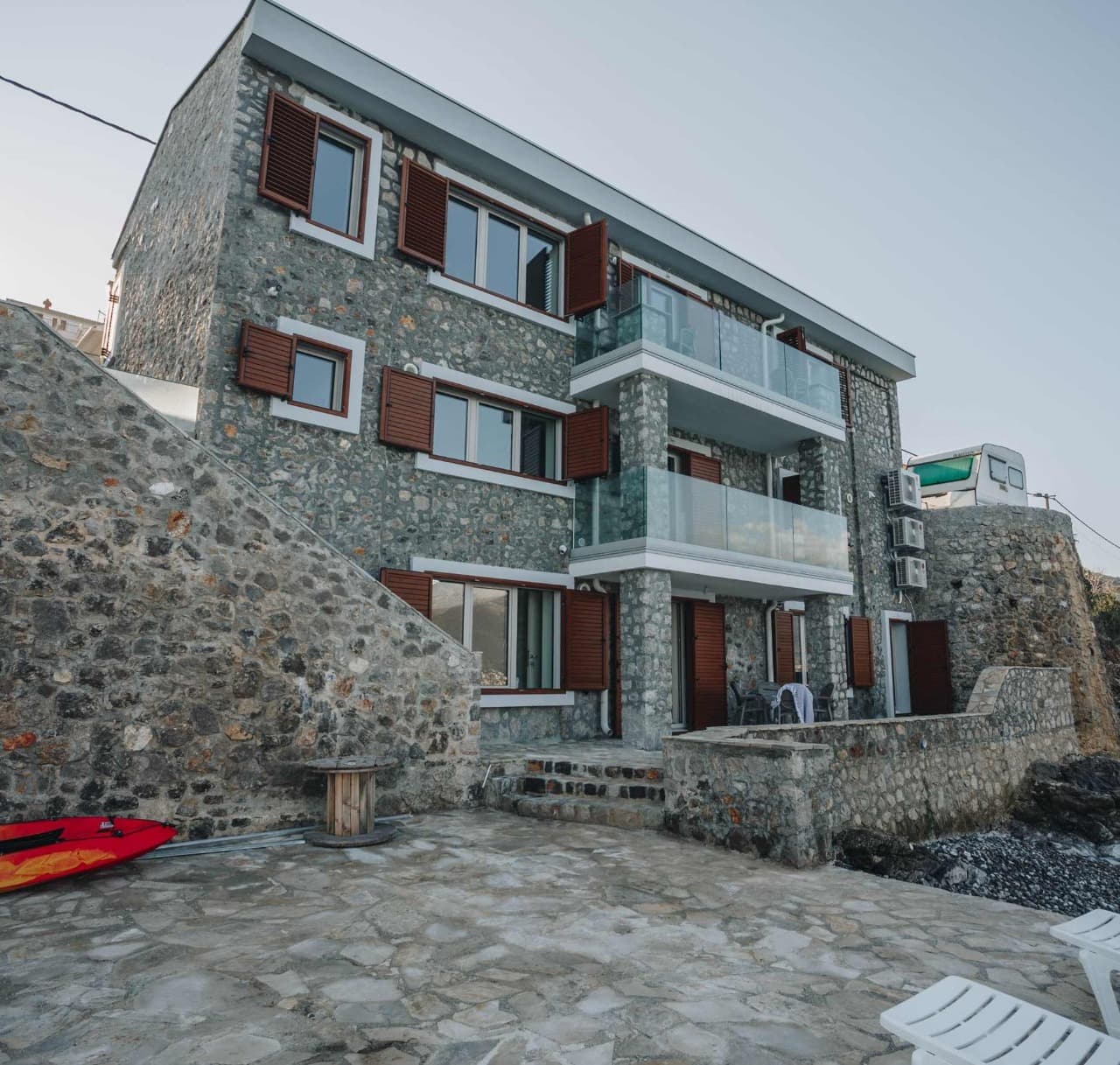 Трехэтажная каменная вилла в Крашичи, Черногория, с террасами, стеклянными ограждениями и видом на море.