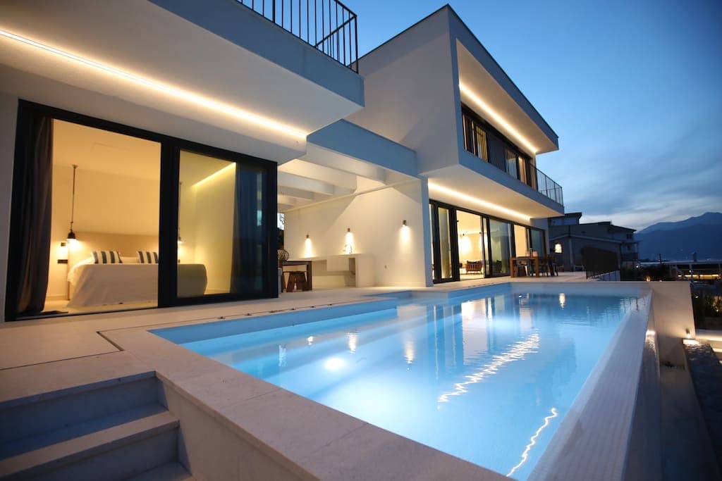 Современная вилла с бассейном и подсветкой фасада на первой линии в Черногории, вид на террасу и спальню вечером.