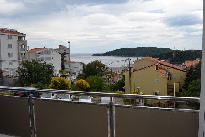 Вид с балкона квартиры в Бечичи, Черногория: панорама на море, горы и жилой район с современной застройкой.