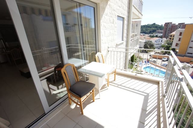 Балкон квартиры в Петроваце, Черногория: столик со стульями, вид на бассейн и город, панорамное остекление.