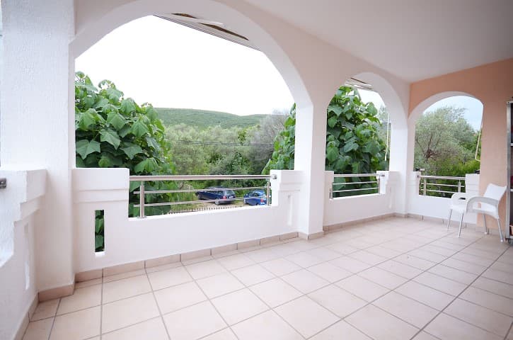 Просторная терраса с арочными проемами и видом на зелень в доме в Крашичи, Черногория. Плиточный пол, белые перила.