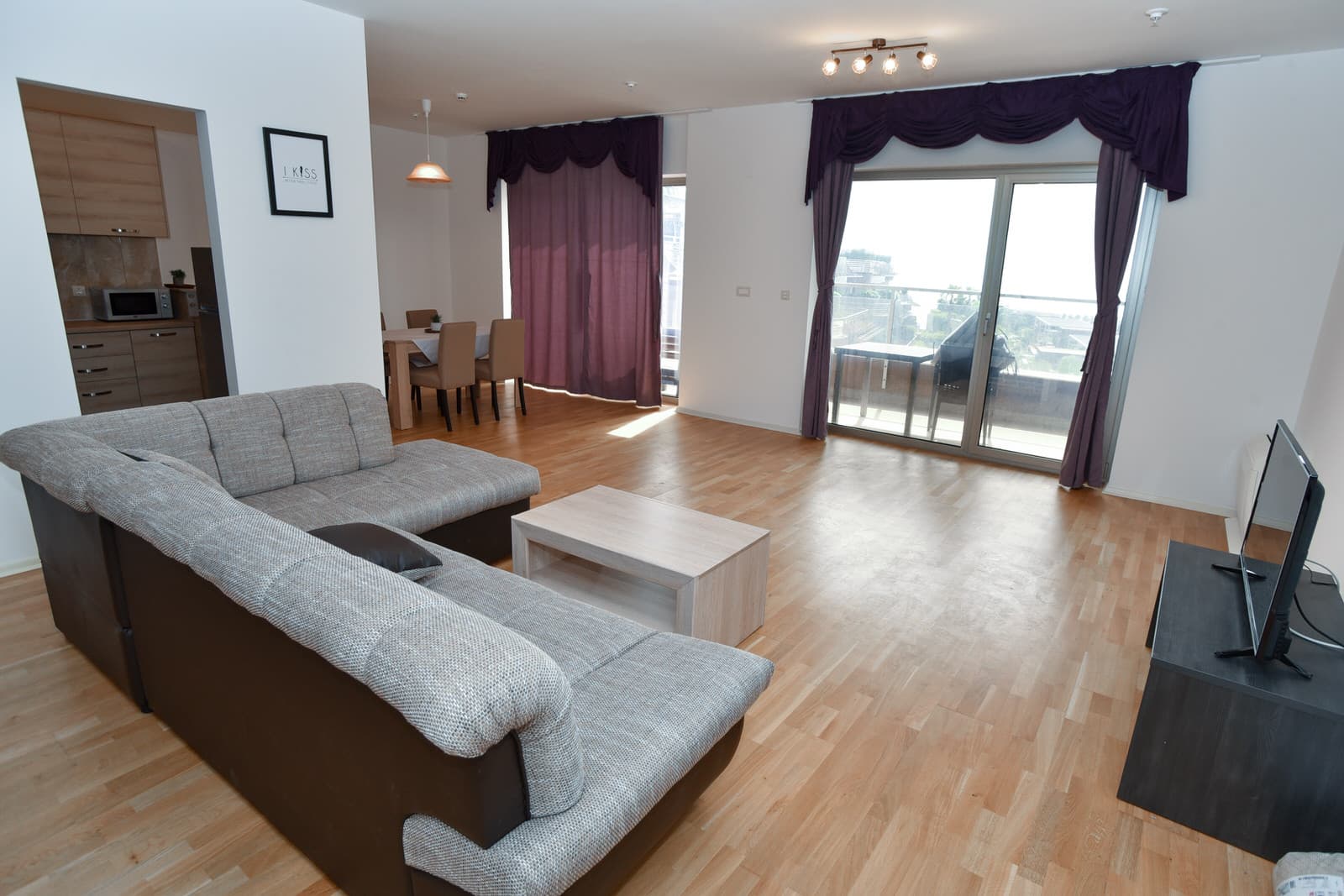 Просторная гостиная с угловым диваном и выходом на террасу в квартире в Будве, Черногория. Современный интерьер с кухней.