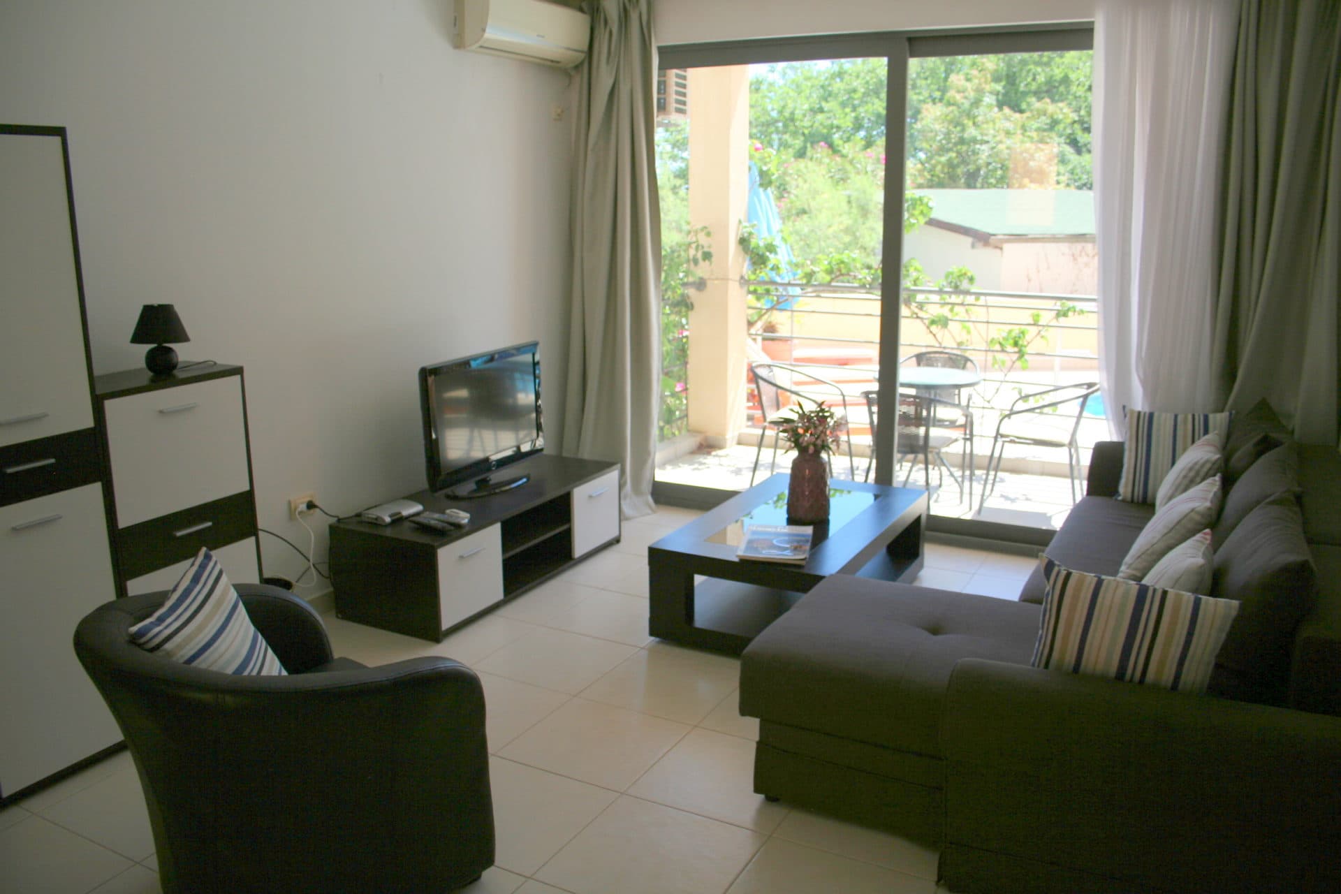 Гостиная в квартире в Бечичи, Черногория: современная мебель, ТВ-зона и выход на террасу с видом на зелень.