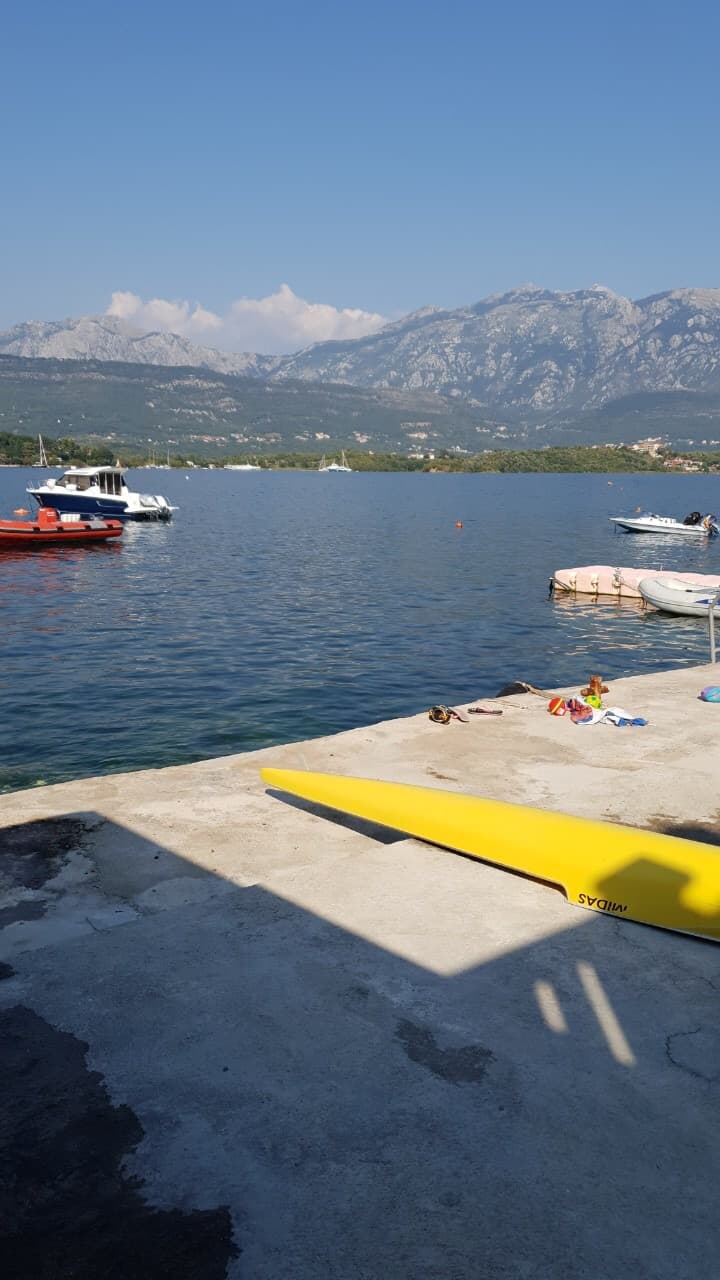 Вид на море и горы с частного причала дома в Тивате, Черногория: желтая лодка на пирсе и катера в бухте.