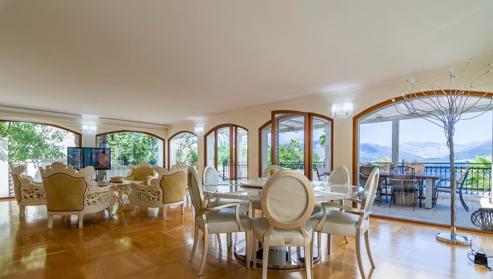 Просторная гостиная с обеденной зоной на вилле в Черногории, панорамные окна с видом на море и горы, классическая мебель.
