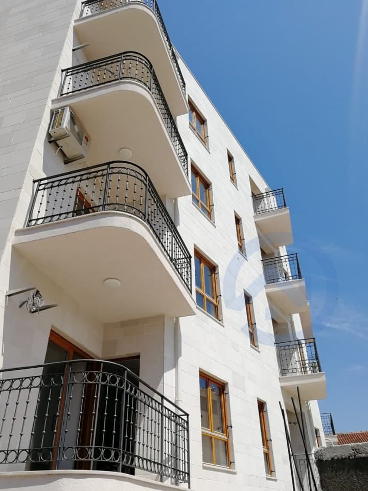 Фасад современного жилого дома с коваными балконами в Петроваце, Черногория. Квартиры в новом здании с отделкой камнем.