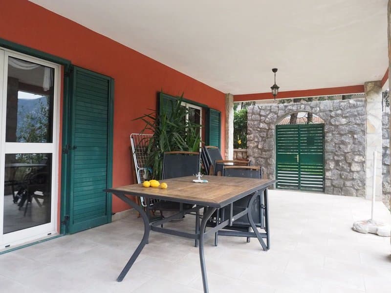 Крытая терраса виллы в Доброте, Черногория: обеденная зона, каменная кладка, зеленые ставни и вид на сад.