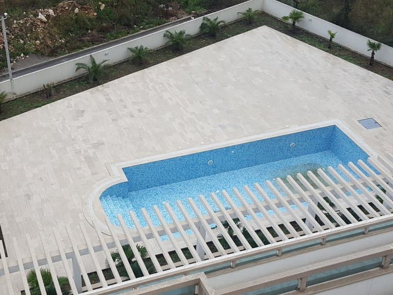 Вид сверху на открытый бассейн с террасой и пальмами у жилого комплекса в Доброте, Черногория.