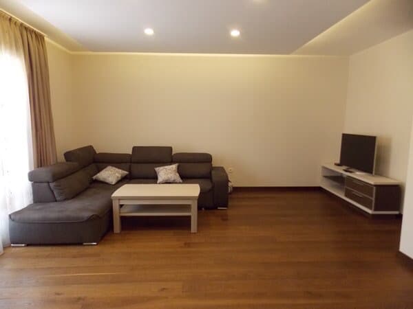 Гостиная в квартире в Будве, Черногория: серый угловой диван, журнальный столик, ТВ-тумба и паркетный пол.