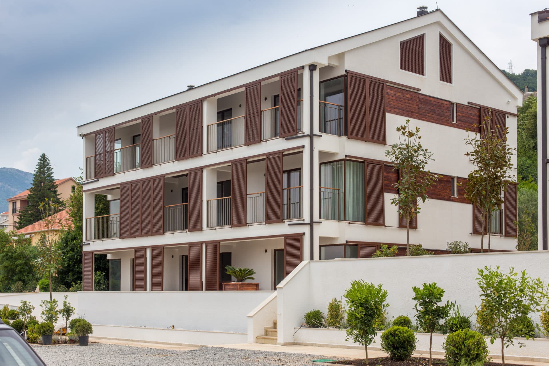 Современный трехэтажный жилой дом с балконами и деревянными ставнями в Тивате, Черногория, с благоустроенной территорией.