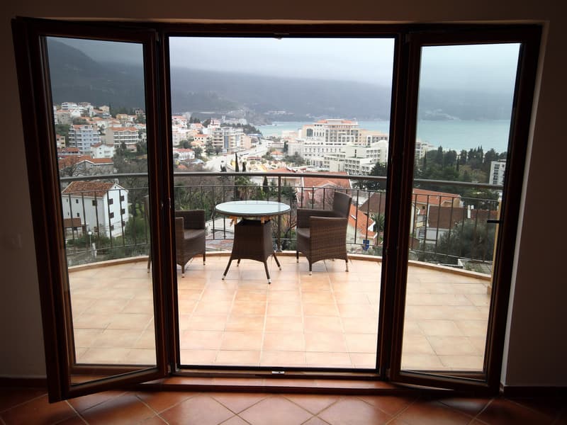 Вид с террасы квартиры в Бечичи, Черногория: плетеная мебель, панорамный вид на море, горы и отели курорта.
