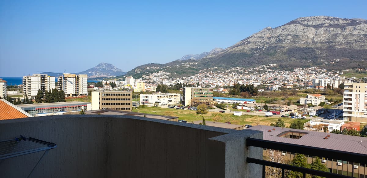 Вид с балкона квартиры в Баре, Черногория: панорама города, горный пейзаж и морское побережье в солнечный день.