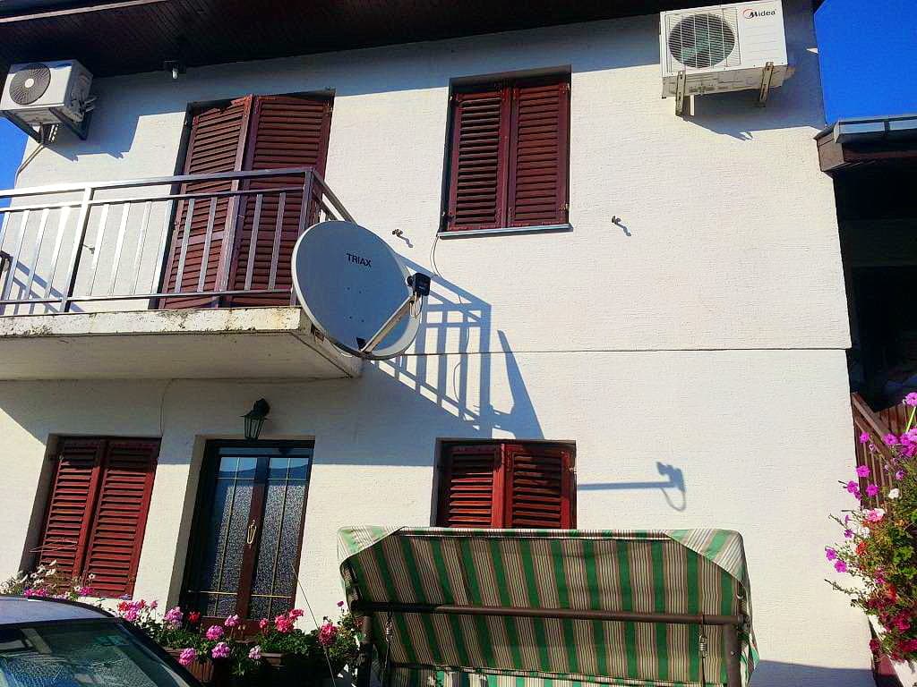 Фасад двухэтажного дома в Герцег-Нови, Черногория: балкон, коричневые ставни, кондиционеры и садовые качели у входа.