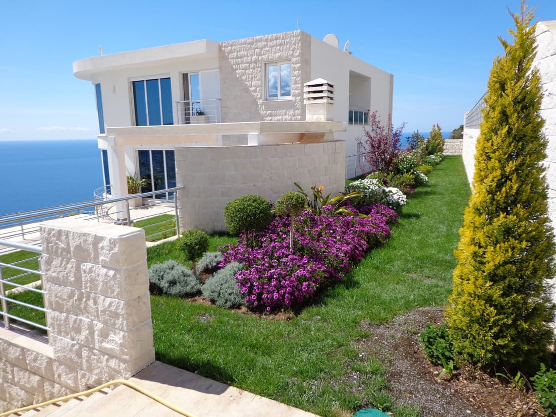 Современная вилла в Добрых Водах, Черногория: каменная отделка фасада, ухоженный сад с цветами и панорамный вид на море.