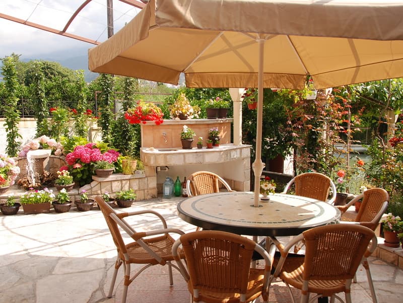 Уютная терраса с плетеными креслами, столом и фонтаном в доме в Игало, Черногория. Летняя зона отдыха в саду.