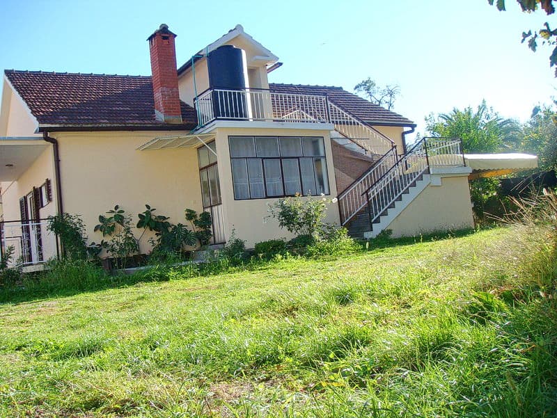 Двухэтажный дом с террасой и садом в Баошичи, Черногория: вид на фасад, внешнюю лестницу и черепичную крышу.