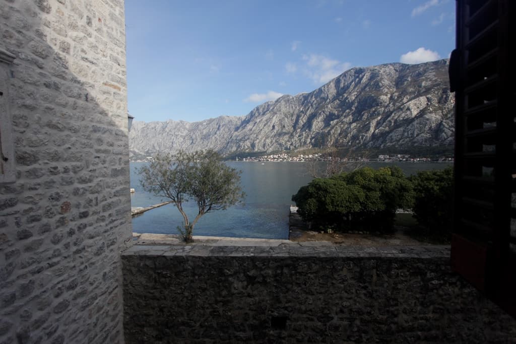 Вид на Которский залив и горы из каменного дома в Прчани, Черногория: терраса с каменной кладкой и панорамный морской пейзаж.