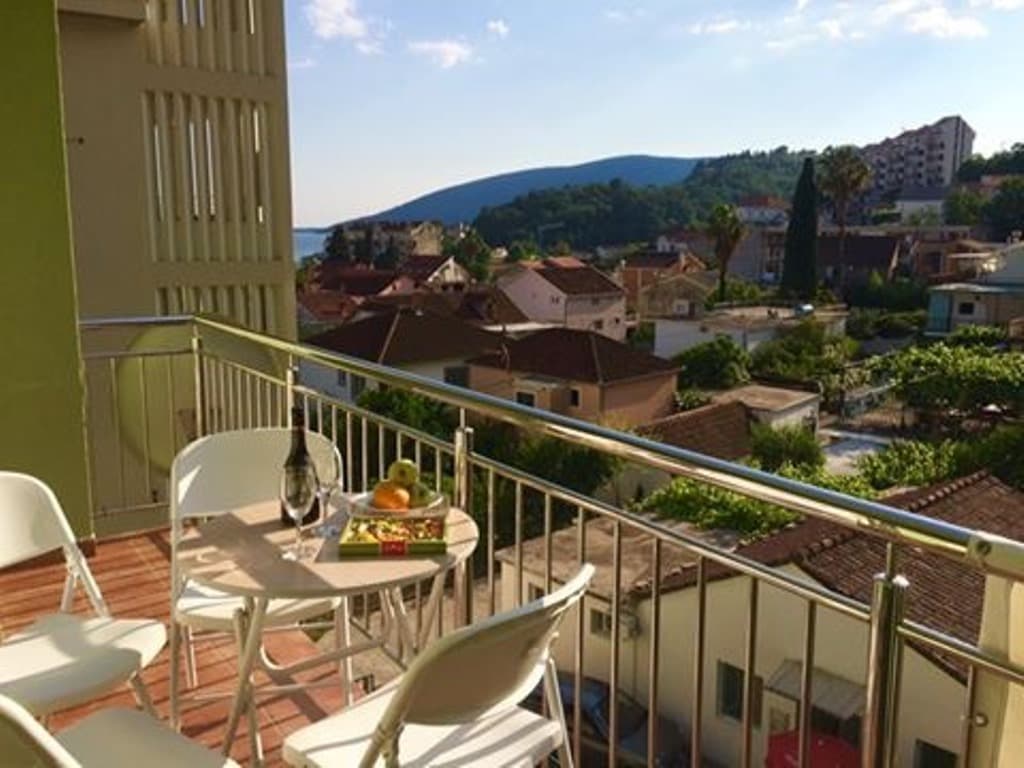 Вид с балкона мини-отеля в Мелине, Черногория: столик с закусками, металлические перила и панорама города с горами.