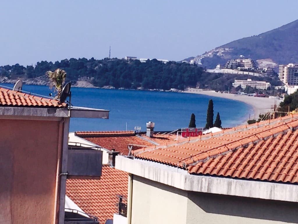 Вид на море и пляж из мини-отеля в Рафаиловичи, Черногория: черепичные крыши домов и панорама побережья.