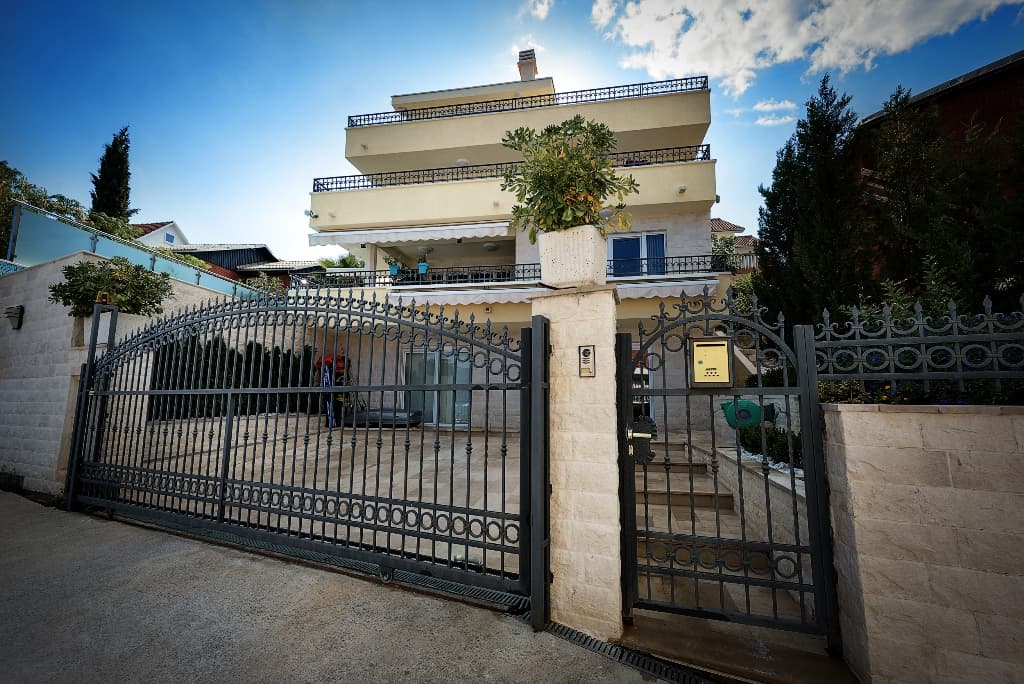 Трехэтажная вилла в Крашичи, Черногория: фасад с коваными воротами, каменной отделкой и террасами на каждом этаже.