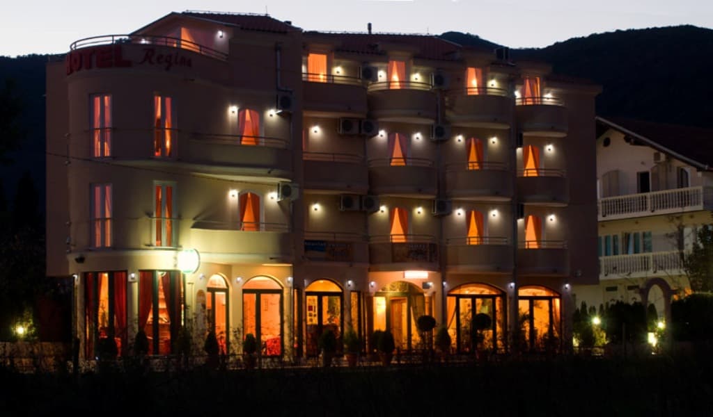 Фасад мини-отеля Regina в Биеле, Черногория: вечерняя подсветка, балконы с кондиционерами и панорамные окна первого этажа.