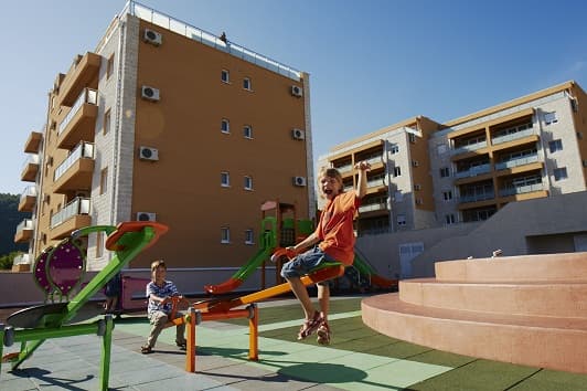 Детская площадка во дворе жилого комплекса с апартаментами в Бечичи, Черногория: современные дома с балконами.