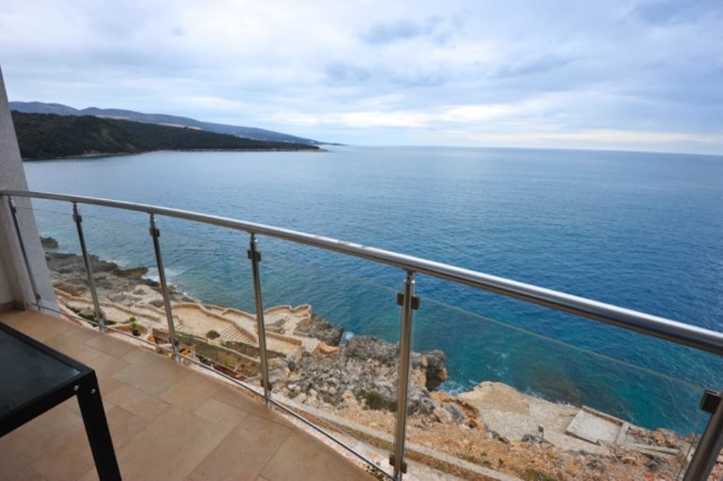 Вид с балкона квартиры в Добрых Водах, Черногория: панорама Адриатического моря, скалистый берег и стеклянное ограждение.