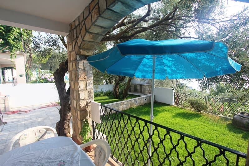 Терраса с каменной аркой и видом на зеленый сад в апартаментах Пржно, Черногория: стол, зонт и уютная зона отдыха.