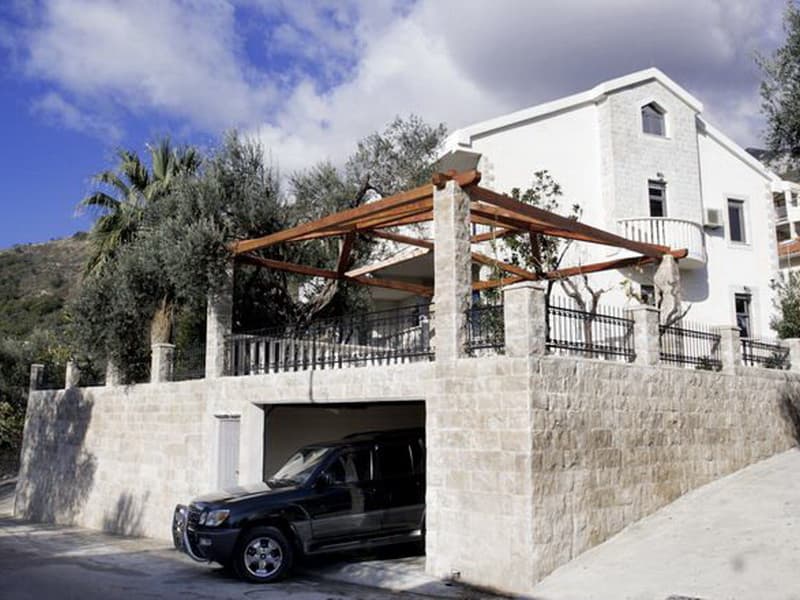 Белая вилла в Петроваце, Черногория: каменная отделка фасада, гараж на первом этаже и терраса с деревянным навесом.