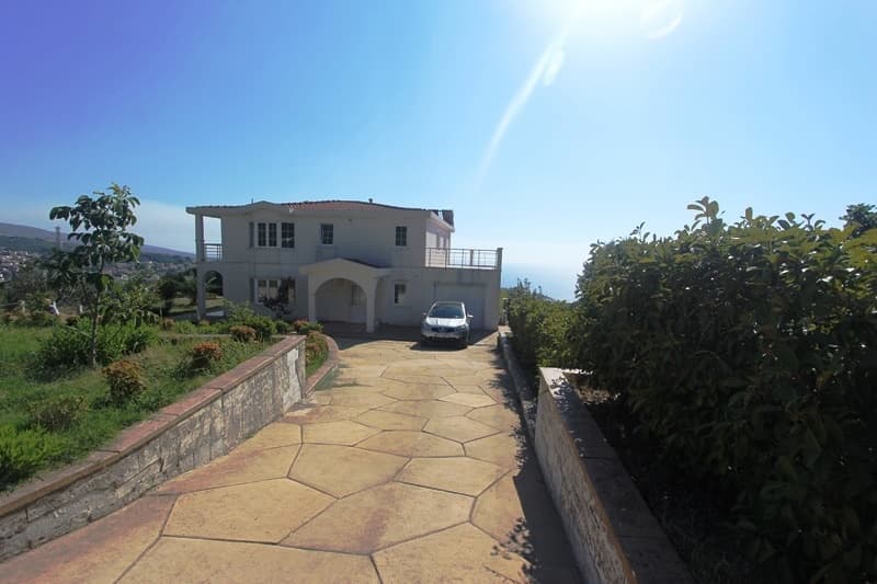 Двухэтажная вилла с гаражом и террасой в Добрых Водах, Черногория: вид на фасад дома и подъездную дорожку из камня.