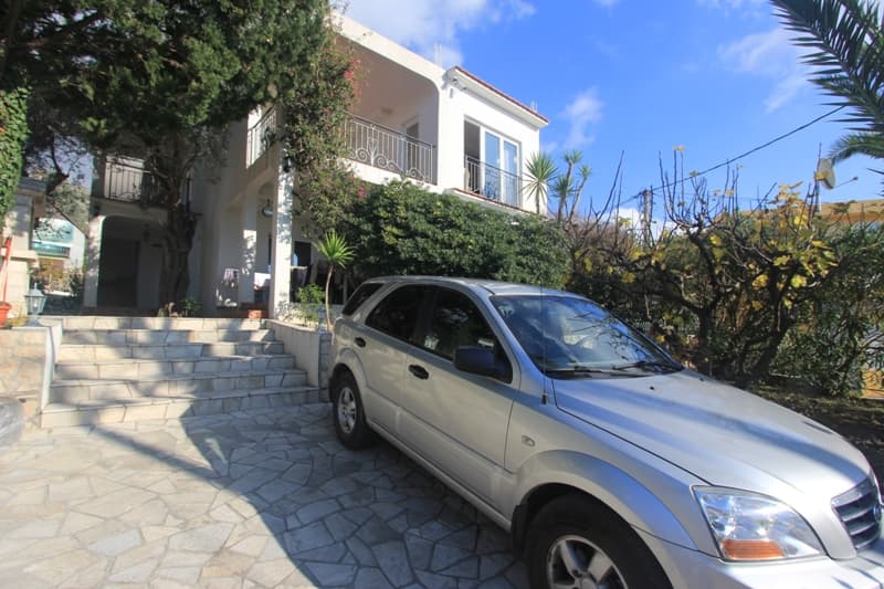 Двухэтажный дом с террасой и парковкой в Шушани, Черногория: фасад здания, каменная лестница и зеленый сад.