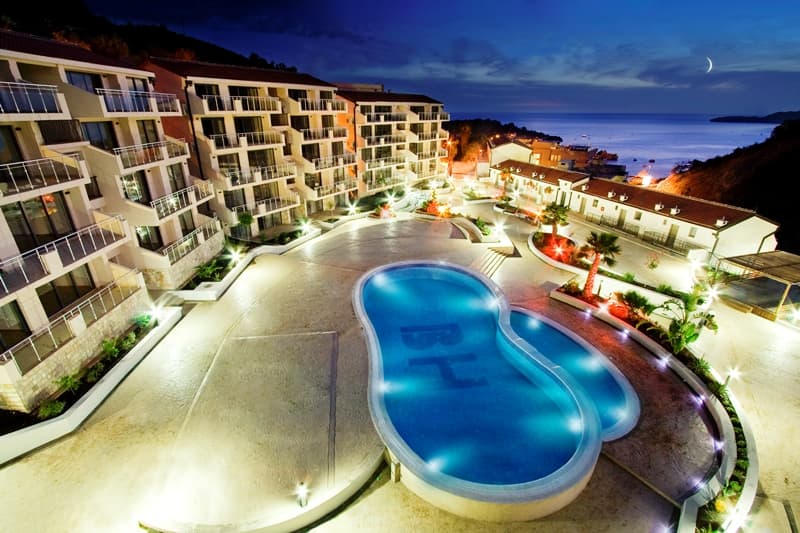 Вечерний вид на жилой комплекс с бассейном и террасами в Пржно, Черногория: современная архитектура у моря.